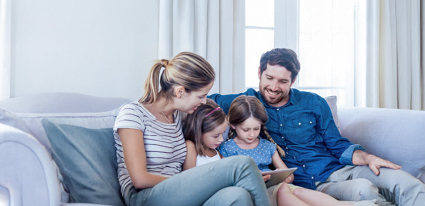 Familie sitzt gemütlich auf einem Sofa und schaut gemeinsam auf ein Tablet.