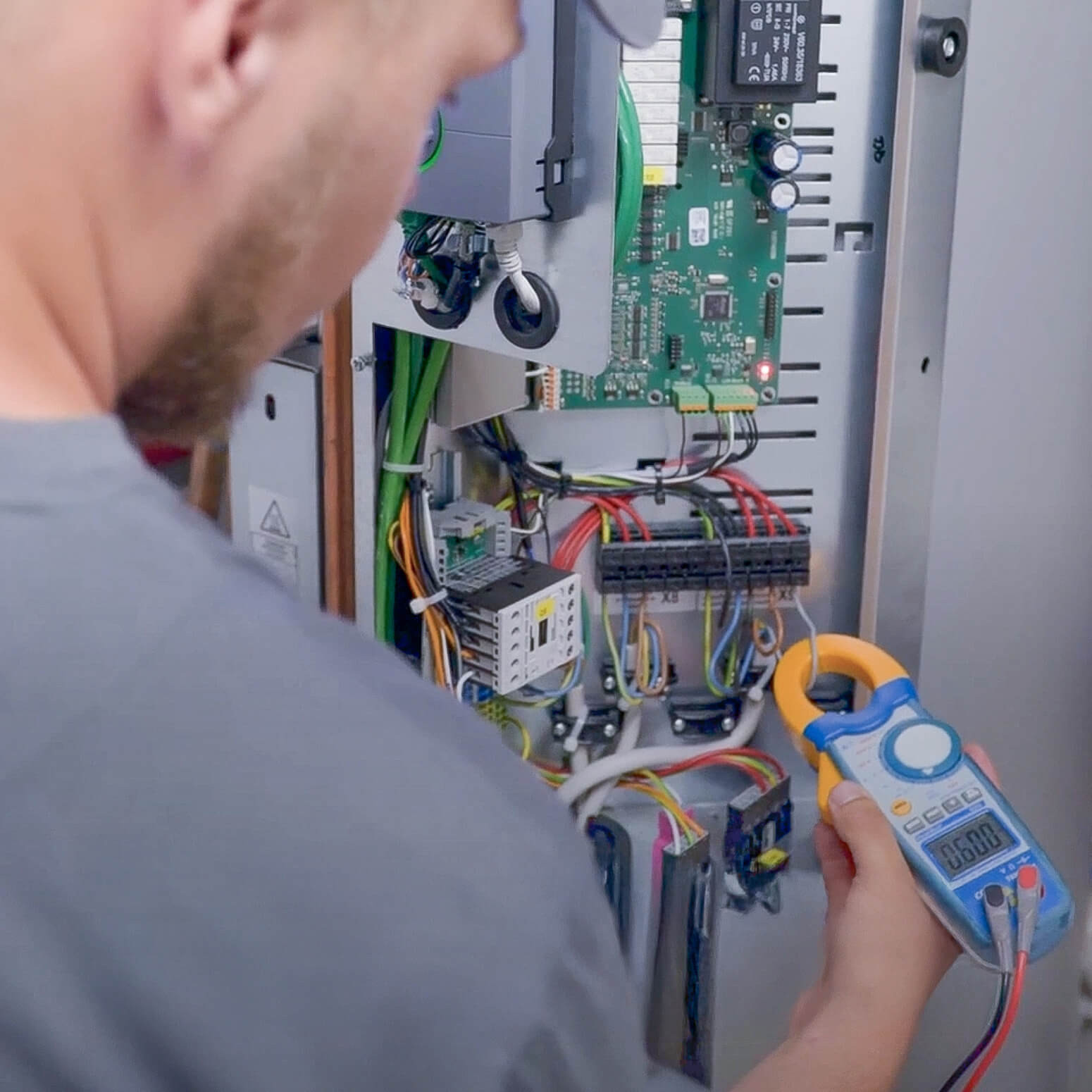 Techniker bei der Arbeit an einem Schaltschrank mit Multimeter zur Messung elektrischer Werte.
